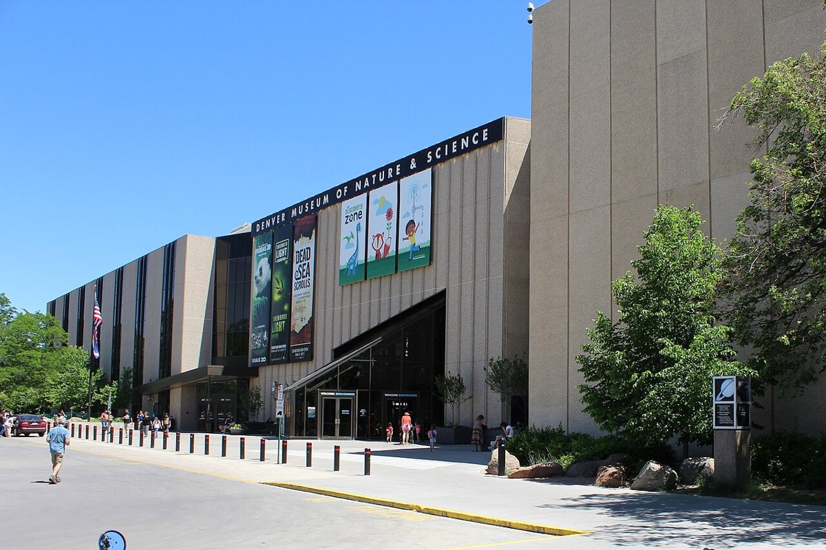 exterior of the Denver Museum of Nature and Science with the Denver skyline and mountains in the background