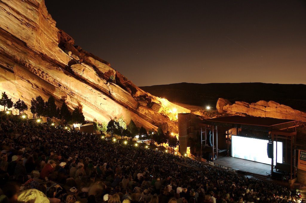 a packed nighttime concert crowd in front of the lit stage and red sandstone at Red Rocks Amphitheatre